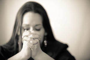 A young woman praying with her hands together on white background